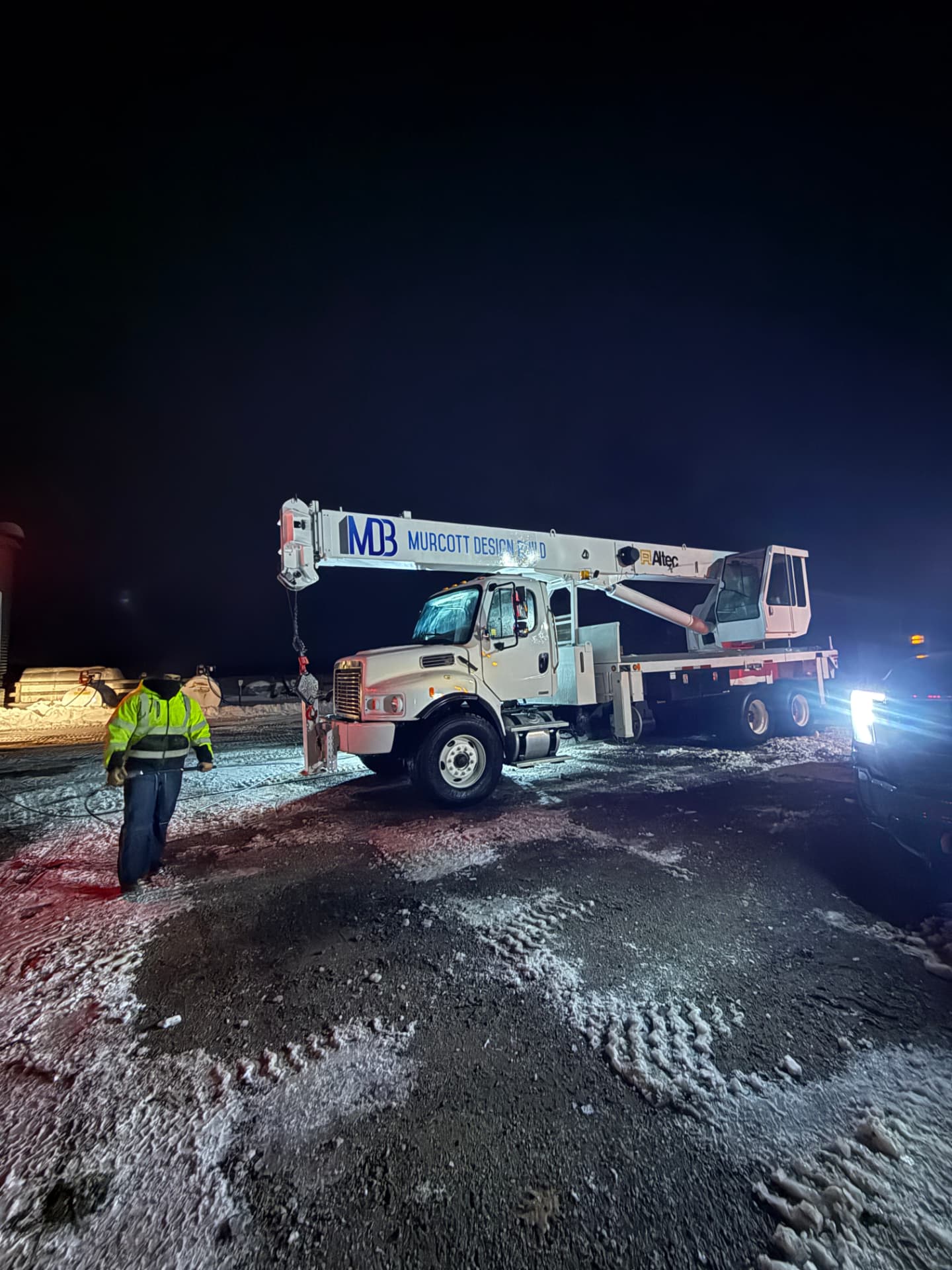 Crane truck being washed at night on a snowy job site by a Refined Mobile Wash crew member